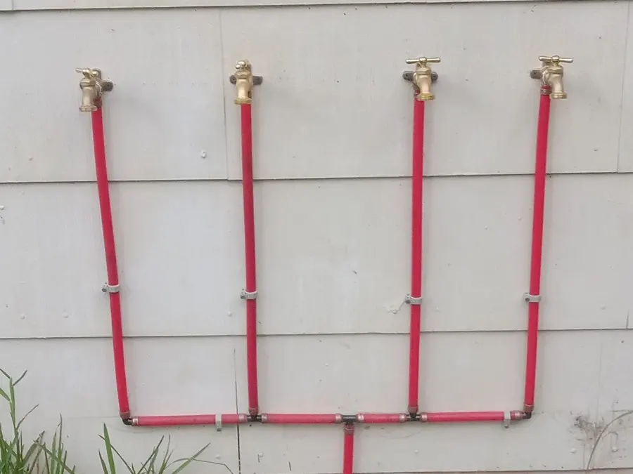 Four red PEX hose bib lines on exterior siding